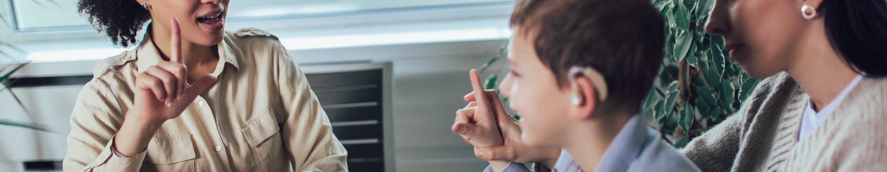 A woman has a sign language conversation with a mother and her hearing impaired son.