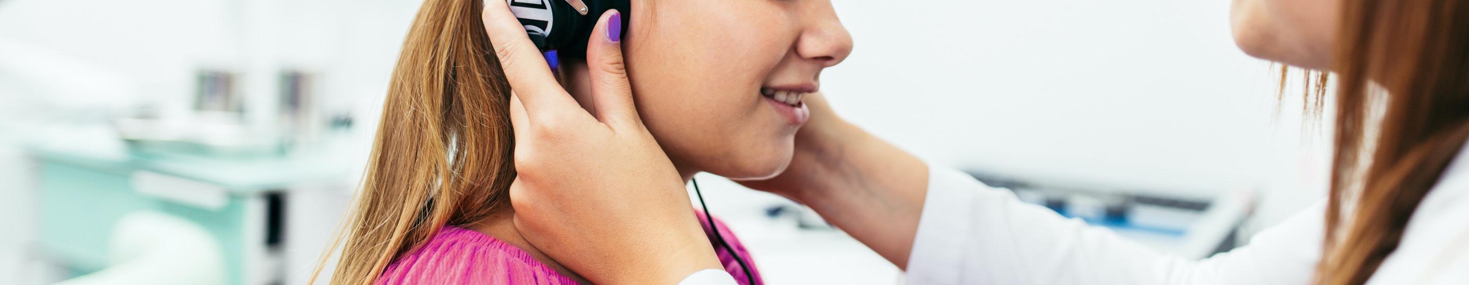 An audiologist places a device around the ears of a young girl.