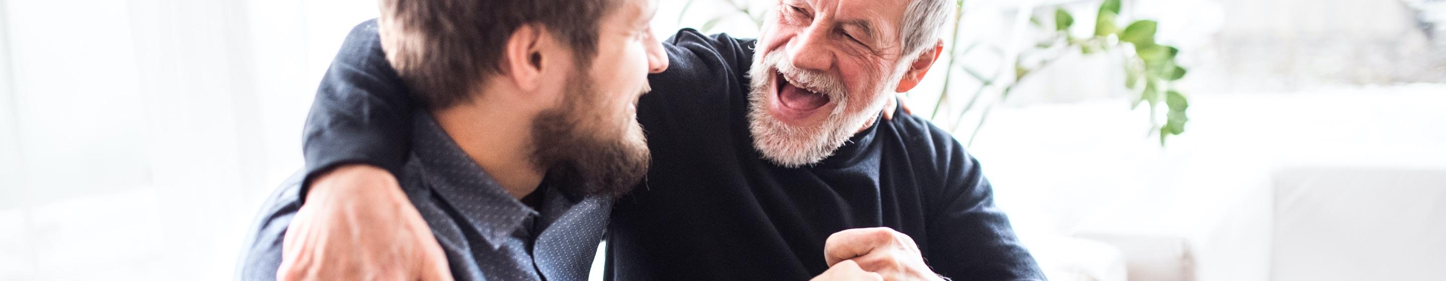 Two bearded men embrace, one older with greying hair, the other a young brunette.